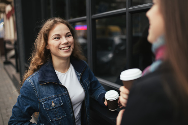 Two young women are happy to drink coffee in city. They holding a paper cups and smiling. - Foto, Imagen