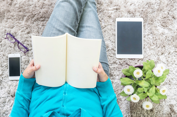 Nahaufnahme asiatische Frau sitzt auf grauem Teppich am Boden im Haus strukturierten Hintergrund für ein Buch in entspannter Zeit mit künstlichen Pflanzen, Tablet, Smartphone und Brille, Freizeit im Haus Konzept - Foto, Bild