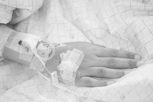 Línea de agua salina de primer plano a la mano del paciente en la cama en la habitación del hospital en tono blanco y negro
 - Foto, imagen