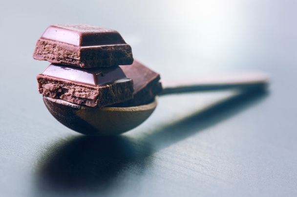 Three bar chocolate on a wooden spoon. Dark blue background.  - Φωτογραφία, εικόνα