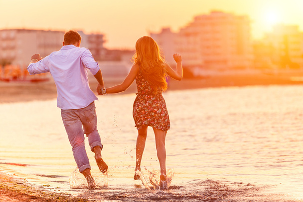 Rear view of happy couple running in summer on the beach in a tropical place. Two lovers in vacation in an idyllic nature scene sharing positive feelings and emotions. Magic moments  of loving hearts. - Photo, Image