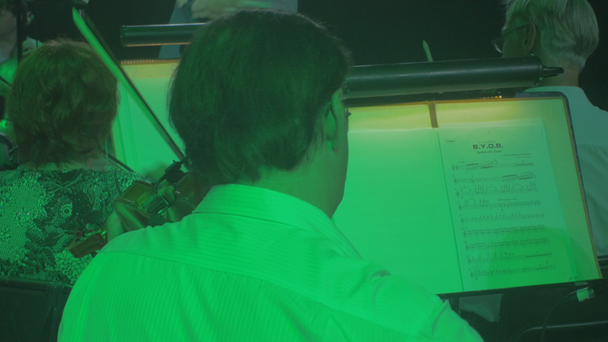 Музиканти грають скрипок репетиція диригент веде рядка сім'ї вклонився інструментів синій і зелений лампи освітлення темному залі книг на трибунах симфонічний рок - Кадри, відео