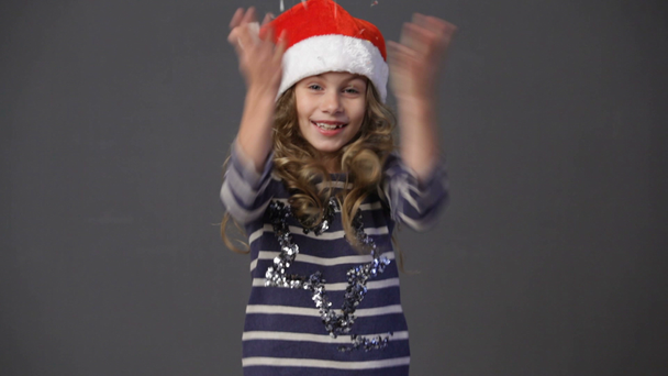 Little girl in a christmas cap throwing up confetti - Záběry, video