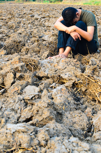 Разочарованный и грустный молодой человек, сидящий на бесплодной земле
 - Фото, изображение