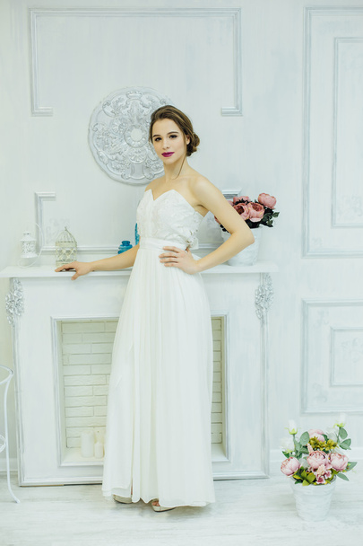 Young bride near the white fireplace. - Фото, изображение