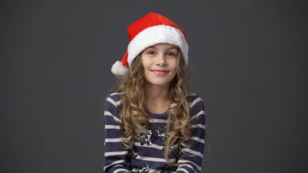 Little girl in a christmas cap throwing up confetti - Materiał filmowy, wideo