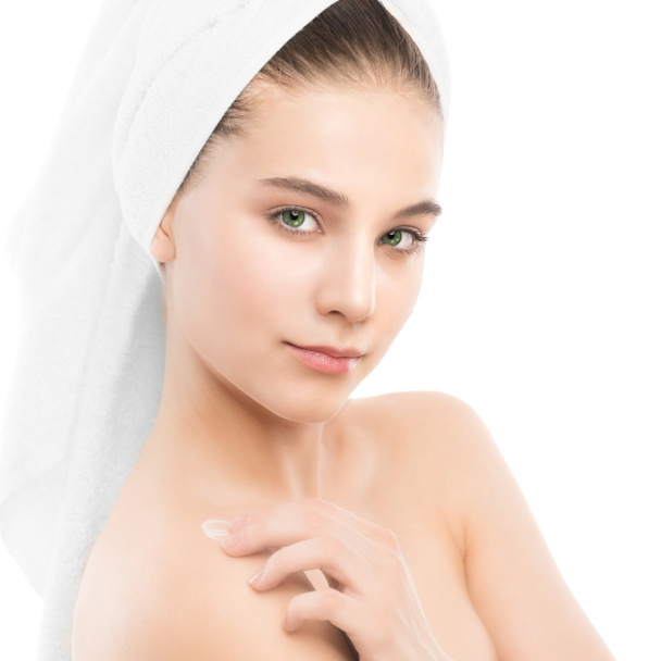 Vrouw met schoon gezicht en handdoek op haar hoofd toepassing moisturizer crème op schouders. Geïsoleerd. - Foto, afbeelding