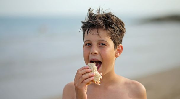 szép fiú, miközben egy szendvicset enni a strandon - Fotó, kép