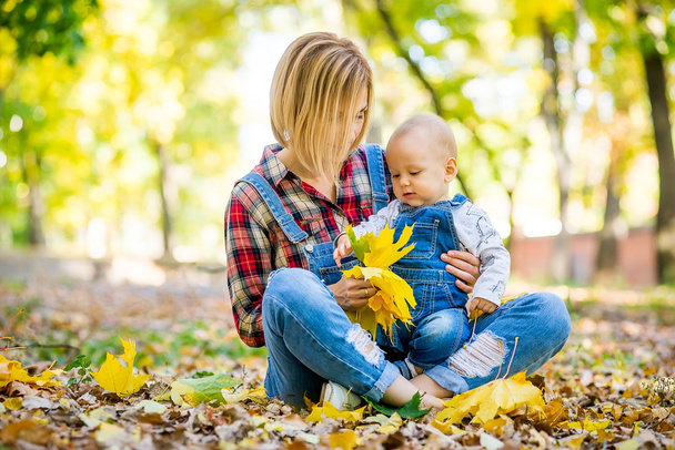 young mother playing with baby in the park in autumn - Foto, afbeelding