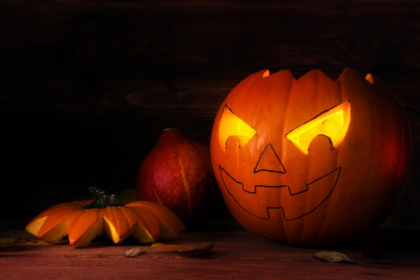 Calabaza de halloween medio tallada con ojos brillantes sobre madera rústica oscura como decoración otoñal
 - Foto, imagen