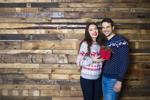 Young couple near wooden wall celebrating Christmas - Photo, Image