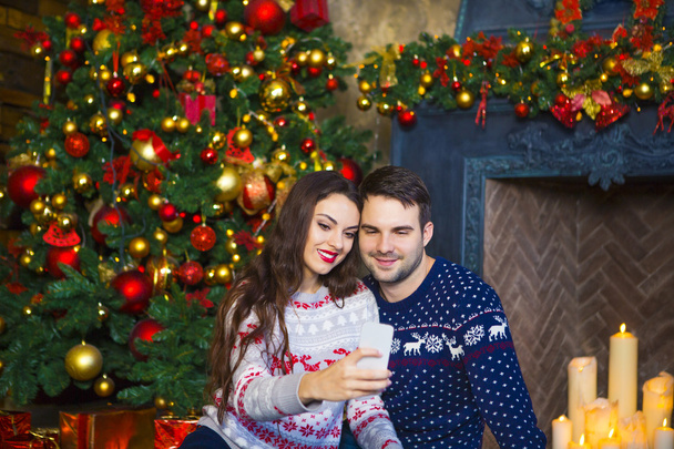 Νεαρό ζευγάρι κοντά στο τζάκι που γιορτάζει τα Χριστούγεννα - Φωτογραφία, εικόνα