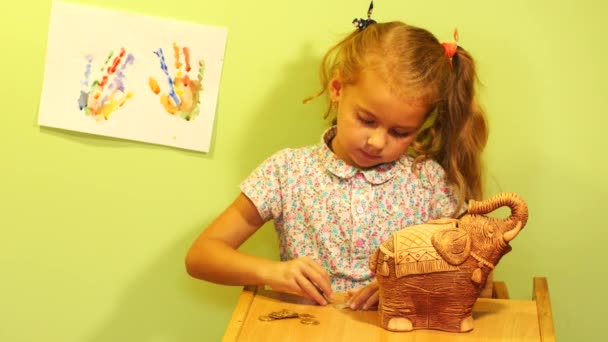 Little girl saving money (coins). Girl insert coins to money box. Cute girl with money box - Záběry, video