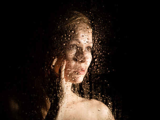 sexy young woman, posing behind transparent glass covered by water drops. melancholy and sad female portrait - Fotografie, Obrázek