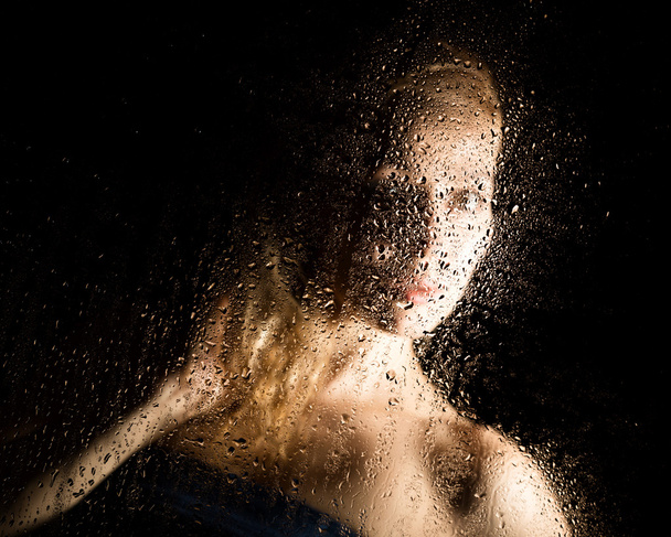 sexy young woman, posing behind transparent glass covered by water drops. melancholy and sad female portrait - Fotoğraf, Görsel