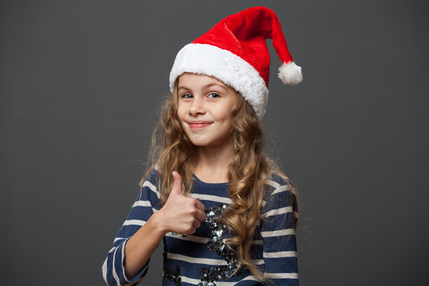 little girl in a christmas cap showing thumb up - Φωτογραφία, εικόνα