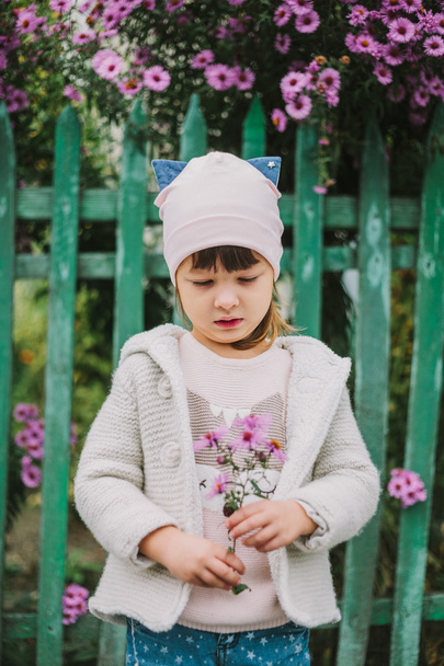 мрійливий портрет маленької дівчинки на фоні паркану і квітів
 - Фото, зображення