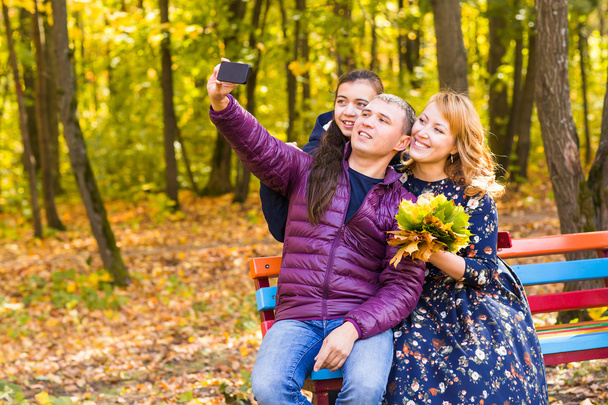 family, childhood, season, technology and people concept - happy family photographing in autumn park - Zdjęcie, obraz