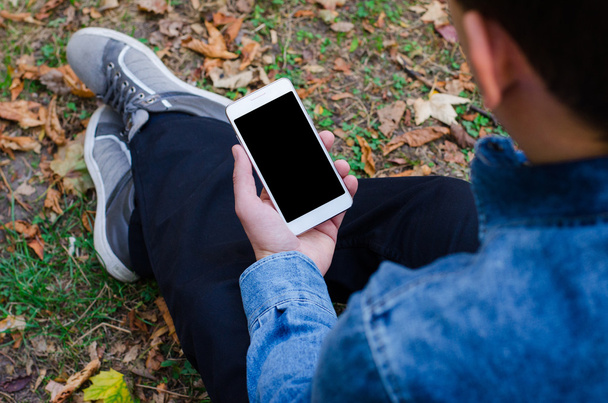 Téléphone portable blanc dans la main un jeune homme d'affaires hipster assis et regardant téléphone portable s d'une dalle de pierre dalles de pavage
 - Photo, image