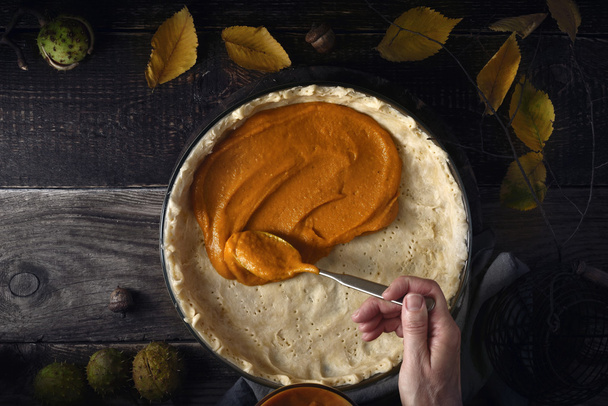 Putting  pumpkin puree on the dough for pumpkin pie on the wooden table - Foto, Imagen