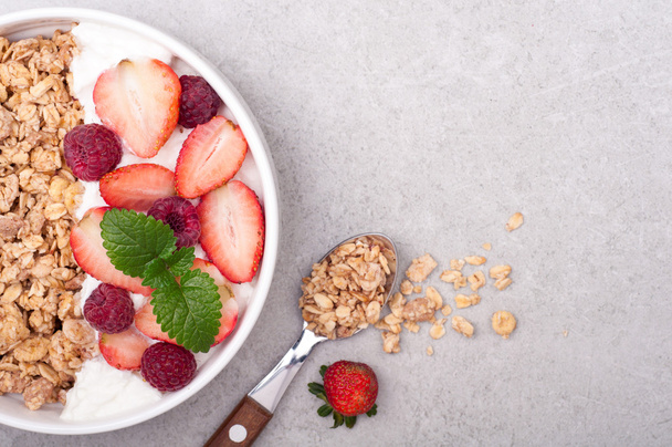 Granola, bogyók és a joghurt, a szürke kő háttér reggelire. Egészséges táplálkozás zabliszt. Szemközti nézet - Fotó, kép
