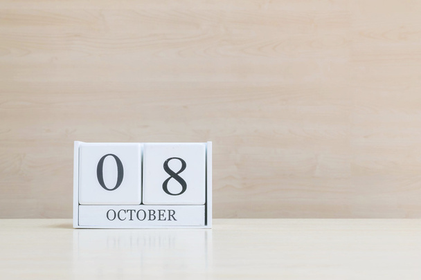 Closeup surface white wooden calendar with black 8 october word on blurred brown wood desk and wood wall textured background with copy space under window light - Photo, Image