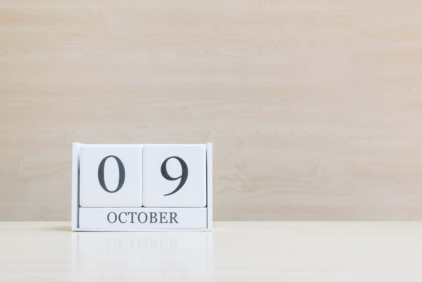 Closeup surface white wooden calendar with black 9 october word on blurred brown wood desk and wood wall textured background with copy space under window light - Photo, Image