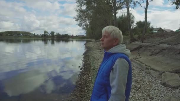 Video van senior man grijze haren kijken naar het meer - Video