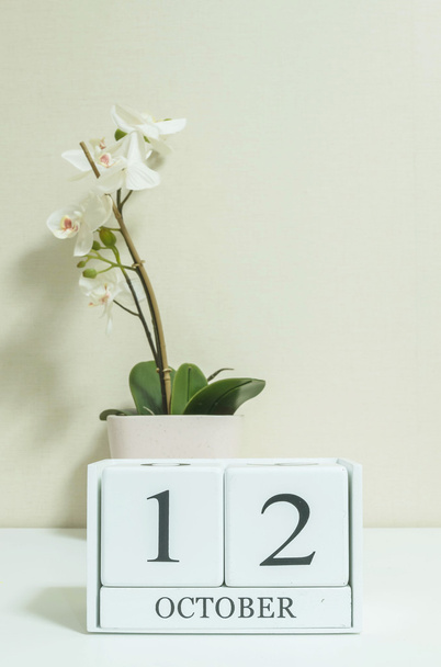 Gros plan calendrier en bois blanc avec noir 12 mot d'octobre avec fleur d'orchidée blanche sur bureau en bois blanc et papier peint de couleur crème dans la chambre fond texturé, voir une autre date dans mon portefeuille
 - Photo, image