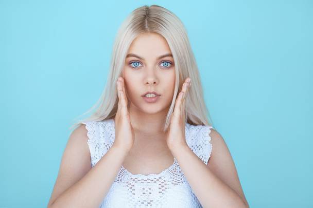 Wide eyed young teenage girl in shock over blue background - 写真・画像