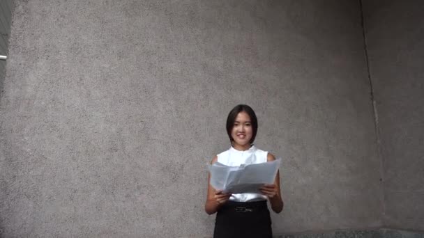 junge schöne Geschäftsfrau weibliches Mädchen Porträt halten werfen Dokumente auf Hintergrund Bürogebäude im Freien - Filmmaterial, Video