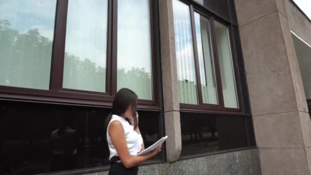 Fiatal gyönyörű üzleti nő női lány portré beszélni a telefont tartsuk dokumentumok séta a háttérben irodaház szabadtéri - Felvétel, videó
