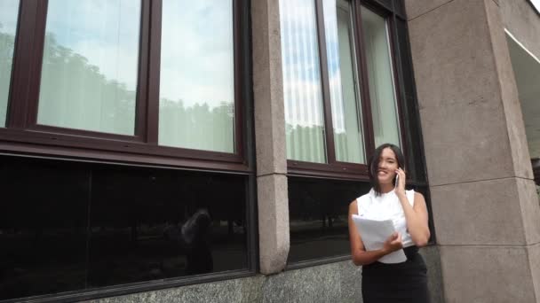 Giovane bella donna d'affari femmina ragazza ritratto parlare su telefono tenere documenti bancarelle su sfondo ufficio edificio all'aperto
 - Filmati, video