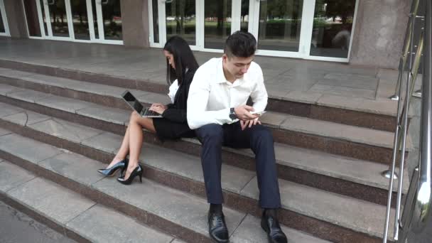 Fiatal gyönyörű üzleti nő nő és kaukázusi Férfi használja hordozható telefon nyomja meg a billentyűzet Sit lépcsőn irodaház - Felvétel, videó