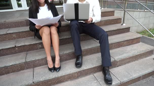 Benen jonge mooie zakenvrouw vrouwelijke en Kaukasische mannelijke gebruik documenten, Laptop pers toetsenbord op de trappen van het kantoorgebouw zitten - Video