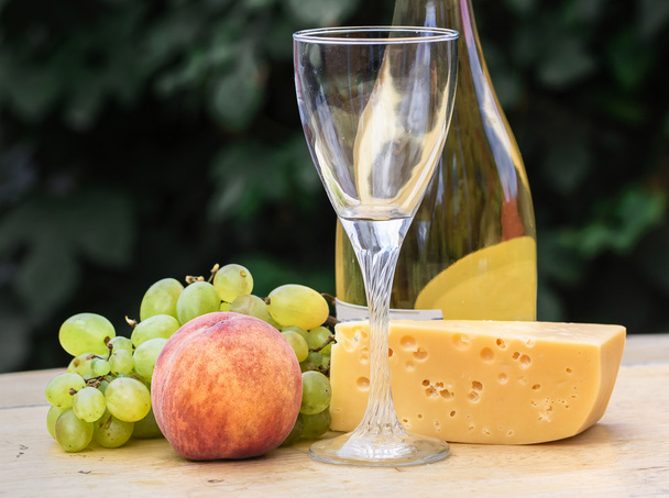 Koostumus juusto, viinirypäleet, persikat, valkoinen, pullot ja lasit viiniä puinen pyöreä pöytä. sisäpihalla
. - Valokuva, kuva