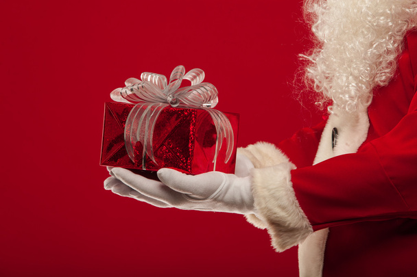 christmas Photo of Santa Claus gloved hand with giftbox, on a red backgro - 写真・画像
