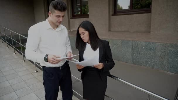 Genç güzel Asya iş kadın erkek ve erkek bakmak beyaz Belgeler Ofis Binası merdivenlerde konuşmak - Video, Çekim