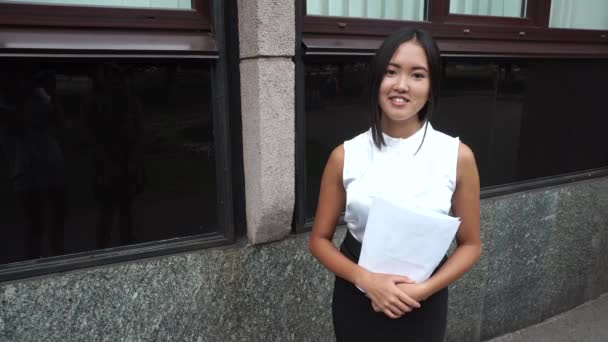 junge schöne Geschäftsfrau weiblich Mädchen Porträt Blick auf Kamera halten Dokumente steht auf Hintergrund Bürogebäude im Freien - Filmmaterial, Video