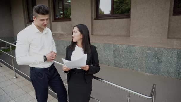 Jonge mooie Aziatische Business vrouw vrouw en Kaukasische mannelijke blik op documenten spreken op kantoorgebouw achtergrond - Video