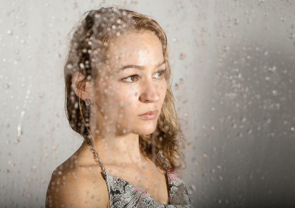 sexy young woman, posing behind transparent glass covered by water drops. melancholy and sad female portrait - Photo, Image