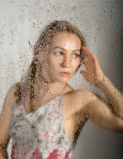 sexy young woman, posing behind transparent glass covered by water drops. melancholy and sad female portrait - Foto, Imagem