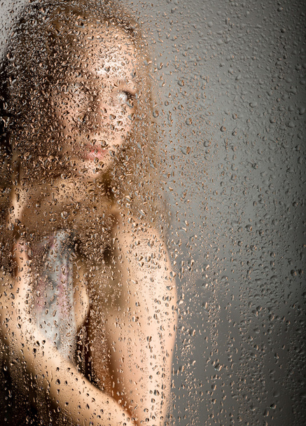 sexy young woman, posing behind transparent glass covered by water drops. melancholy and sad female portrait - Foto, imagen