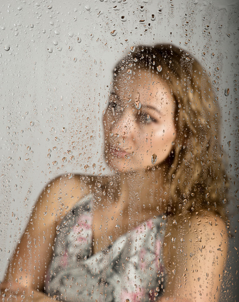 sexy young woman, posing behind transparent glass covered by water drops. melancholy and sad female portrait - Valokuva, kuva