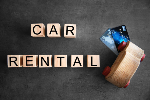 Cubes with words CAR RENTAL and wooden toy on grey background, top view - Photo, image