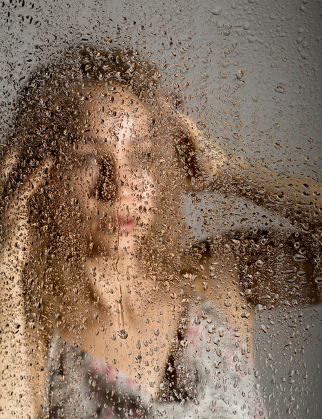 sexy young woman, posing behind transparent glass covered by water drops. melancholy and sad female portrait - Foto, Bild