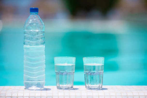 Bicchieri di acqua e bottiglia sul bordo della piscina a sfioro
 - Foto, immagini