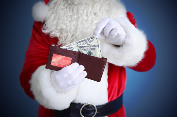 Santa Claus hands holding wallet with money and credit card on blue background - Фото, зображення