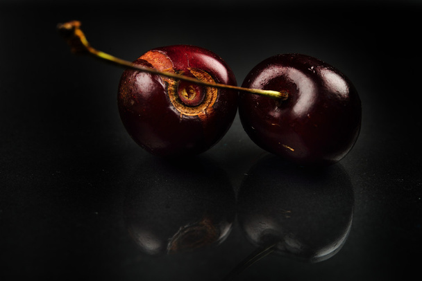 Close up of image of rotten red cherries fruit on reflective bla - Фото, изображение
