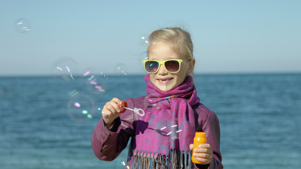 Kabarcıklar deniz sahilde üfleme güneş gözlüklü kız. Kameraya bakarak çocuk - Video, Çekim
